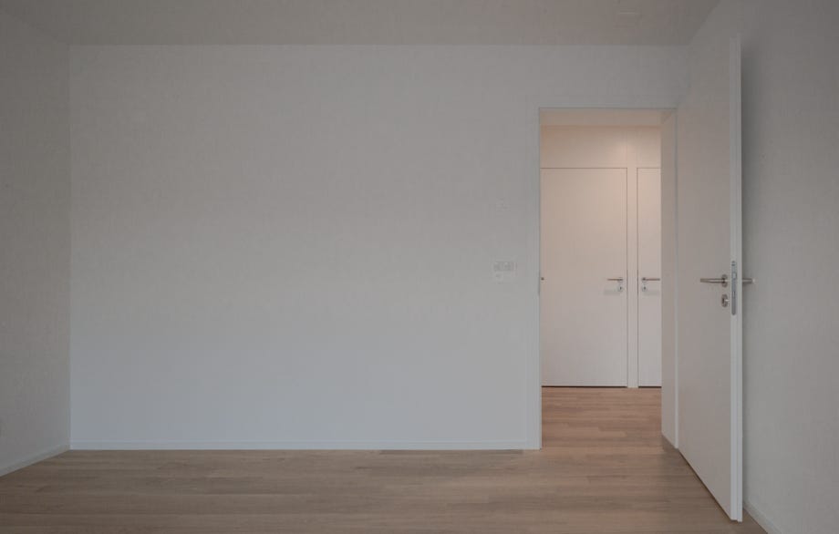 Innenansicht Zimmer mit Tür und Einbauschränken im Vorraum. Hansjörg Betschart Architektur ©.